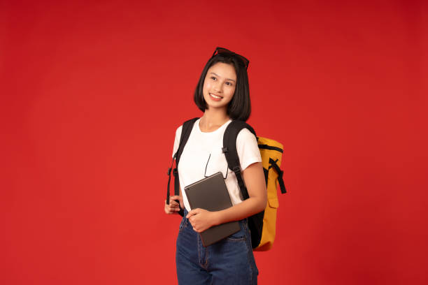 istock A short-haired Asian female student poses in a studio against a red background, effectively conveying her commitment to her studies, using her laptop to study and focus on her academics. 2163899735