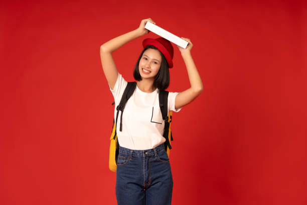 istock Knowledge is a tool for creating change for an Asian female student. She can contribute to society through her experiences and insights from university. Photo taken in a studio with a red background. 2163900514