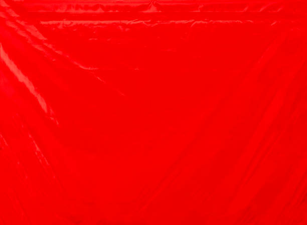 Close up of a bright red  canvas cover with some diagonal and horizontal wrinkles. It was used to cover a trailer. Horizontal orientation. The image has been shot full frame and close up. Ideal for backgrounds.