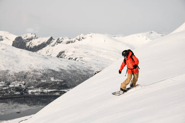 Side view of a snow-covered hill on which a skier in an orange jacket is going down on a split board