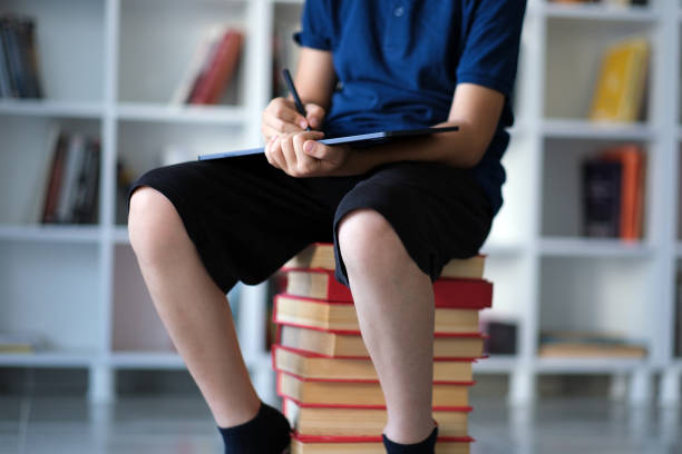 Little Boy Sitting On Books And Holding Digital