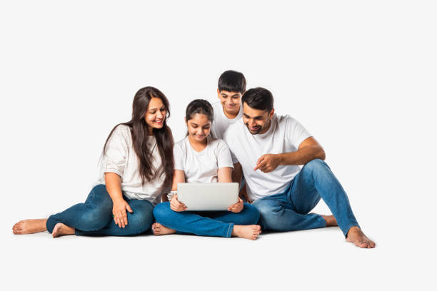 istock Indian asian young family of four using laptop computer while lying on floor or sitting isolated on white 2163920201