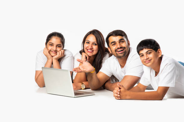 istock Indian asian young family of four using laptop computer while lying on floor or sitting isolated on white 2163920254