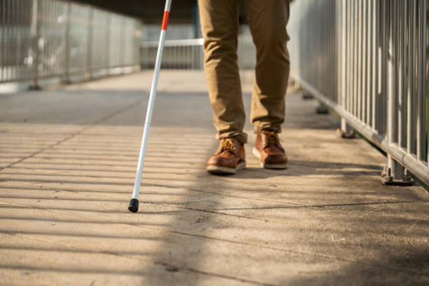 Young blind man walking in city with walking stick. Visually impaired man difficult to traveling on the road wearing sun glasses Cross the road cross the footbridge