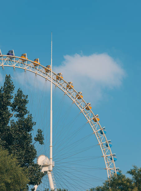 A towering roller coaster reaching its peak against a backdrop of blue sky and fluffy clouds. The structure is metallic and intricate, showcasing the thrill of amusement parks.