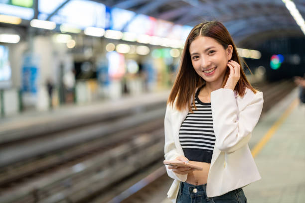 istock Young asian woman using smartphone application navigate location destination while travel by train. Asian female with cell phone standing near railway platform in train station. 2163924244