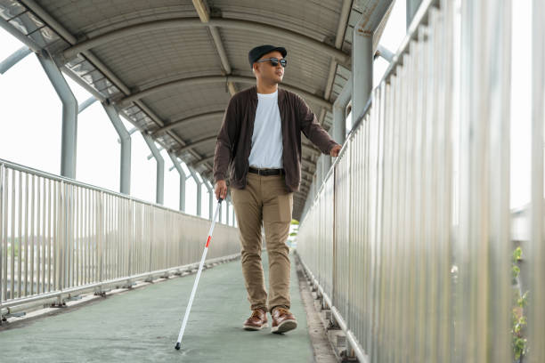 istock Young blind man walking in city with walking stick. Visually impaired man difficult to traveling on the road wearing sun glasses Cross the road cross the footbridge 2163924646