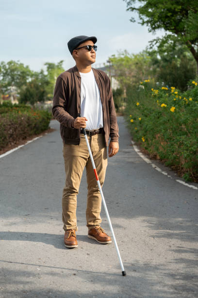 istock Young blind man walking in city with walking stick. Visually impaired man difficult to traveling on the road wearing sun glasses Cross the road cross the footbridge 2163925000