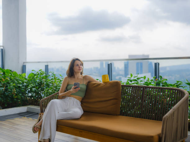 Woman using smartphone drinking coffee on rooftop garden