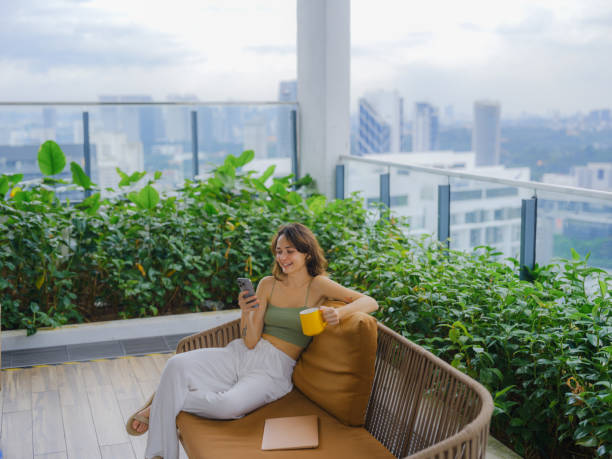 istock Woman using smartphone drinking coffee on rooftop garden 2163927318