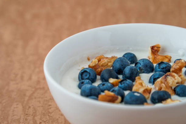 Concept photo of a yoghurt with fresh blueberries and walnuts on a brown background with text space