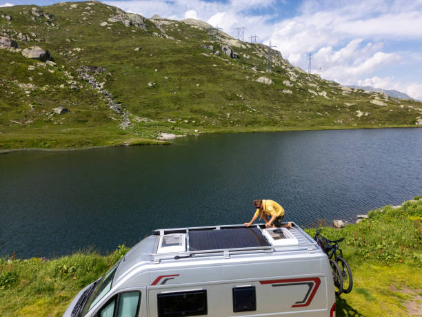 istock Man Maintaining Solar Panels on Camper Van Roof by Lake 2163940457