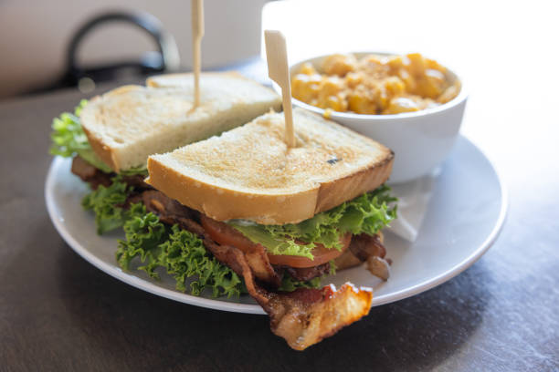 A BLT sandwich with bacon, lettuce and tomato sits on a white plate next to a bowl of macaroni and cheese