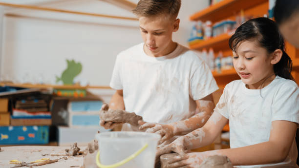 istock Boy modeling bowl of clay while cute asian girl working on dough. Edification. 2163951590