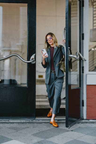 istock Businesswoman Using Smartphone While Leaving Modern Office Building 2163968633