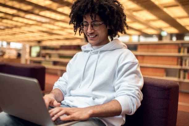 istock Male student engaged in online studying working on diploma project using laptop in library campus 2163969858