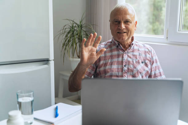 istock Senior man waving at laptop screen, indoor setting. 2163971877