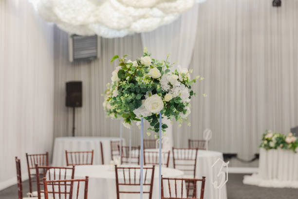 istock Decorated interior for festive event. Fancy table set for dinner with white flower composition in restaurant, luxury interior background. Wedding elegant banquet decoration arranged by catering service. 2163973796