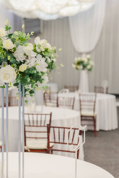 istock Decorated interior for festive event. Fancy table set for dinner with white flower composition in restaurant, luxury interior background. Wedding elegant banquet decoration arranged by catering service. 2163973801