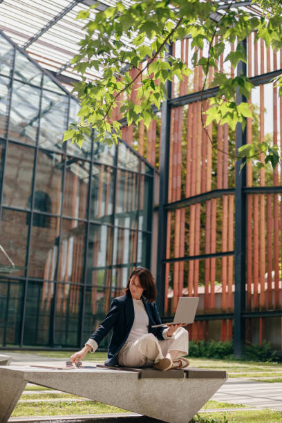 istock Woman working outdoors on laptop in modern office atrium, blending nature and technology 2163978834