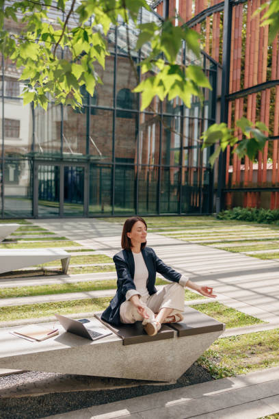 istock A woman is peacefully meditating outdoors on a bench in a modern office courtyard 2163979419