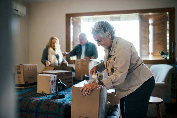Group of senior friends unpacking boxes in the bedroom Group of senior friends unpacking boxes in the bedroom, while having conversations and smiling seniors-moving-house stock pictures, royalty-free photos & images