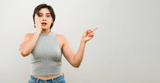 istock Shocked young woman points at something surprising while covering her face with her hand 2163983091