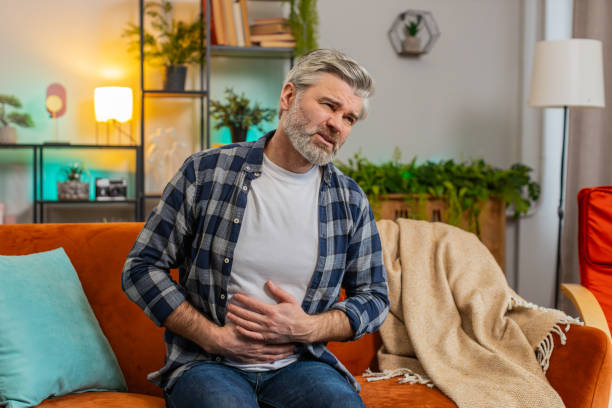 istock Senior middle-aged man sits on couch feeling sudden strong abdominal stomach ache gastritis problem 2163983259