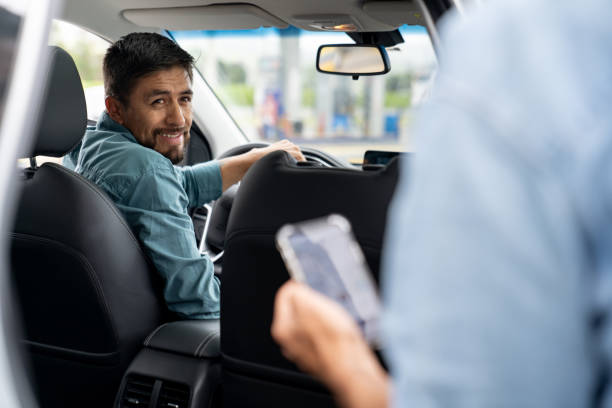 Crowdsourced taxi driver picking up a passenger Latin American crowdsourced taxi driver picking up a passenger and smiling - mobility as a service concepts man looking at phone over shoulder stock pictures, royalty-free photos & images
