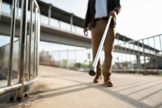 Young blind man walking in city with walking stick. Visually impaired man difficult to traveling on the road wearing sun glasses Cross the road cross the footbridge