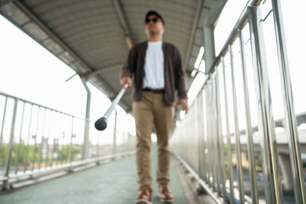Young blind man walking in city with walking stick. Visually impaired man difficult to traveling on the road wearing sun glasses Cross the road cross the footbridge