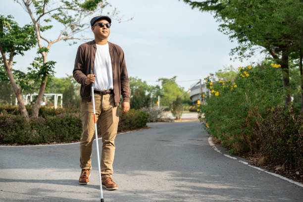 istock Young blind man walking in city with walking stick. Visually impaired man difficult to traveling on the road wearing sun glasses Cross the road cross the footbridge 2163997654