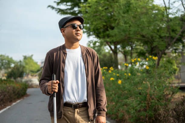 Young blind man walking in city with walking stick. Visually impaired man difficult to traveling on the road wearing sun glasses Cross the road cross the footbridge