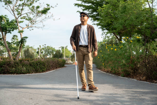 istock Young blind man walking in city with walking stick. Visually impaired man difficult to traveling on the road wearing sun glasses Cross the road cross the footbridge 2163998483