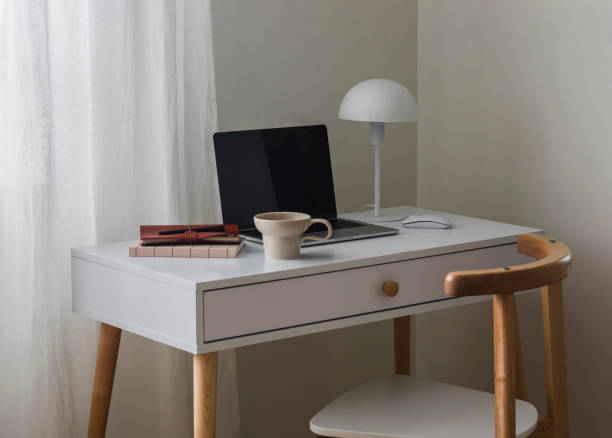 istock A laptop, notebooks, a cup of coffee, a table lamp on a white table by the window - a minimalistic style workplace for work, learning, communication 2164000076