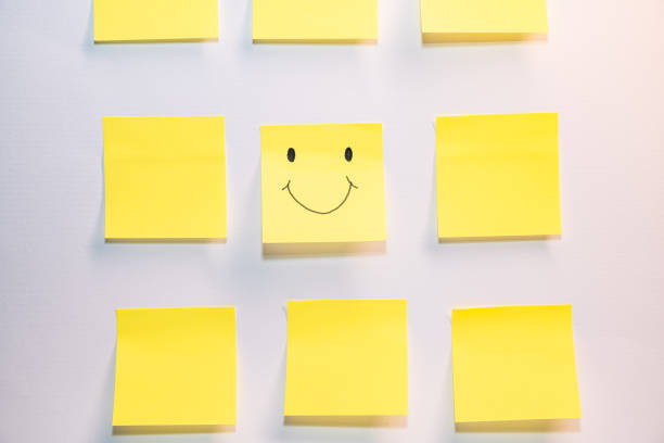 A yellow smiley face is drawn on a sheet of paper and is surrounded by other pieces of paper