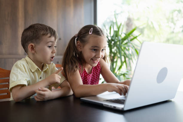 Older sister helping younger brother with homework on a laptop, demonstrating teamwork and support