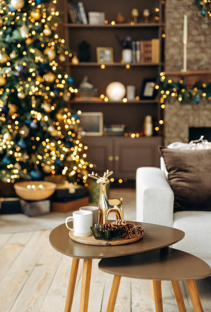 istock A coffee table with Christmas decor on a blurred background of a sofa and a Christmas tree with garland lights in the cozy room with a fireplace and New Year's decor. Christmas deer and fir cones 2164013474