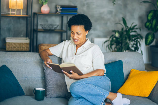 istock Woman relaxing at home reading a book lying on sofa 2164015794