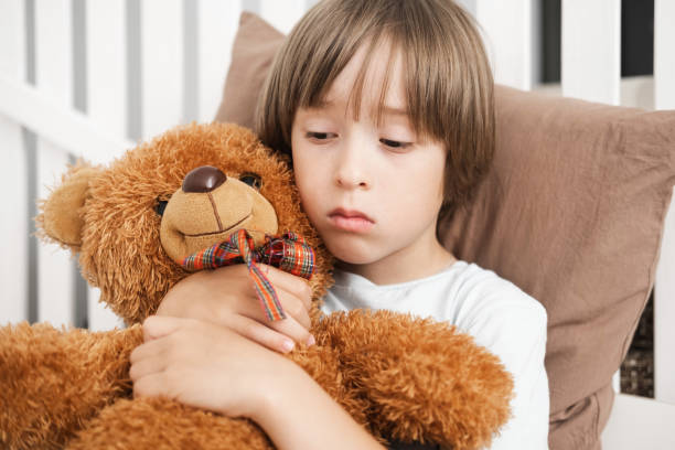 istock A sad, upset little boy is lying on the bed and hugging his teddy bear. 2164022906
