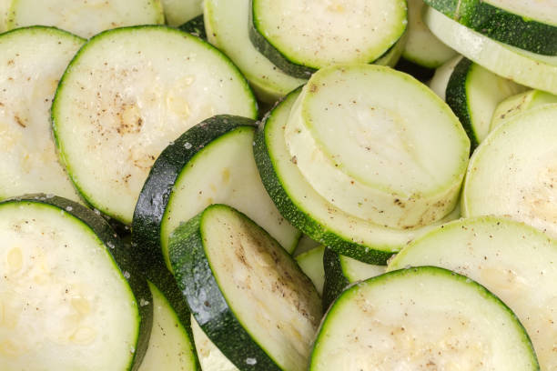 Raw green zucchini and white vegetable marrow sliced into circles and sprinkled with salt and spices, close-up in selective focus