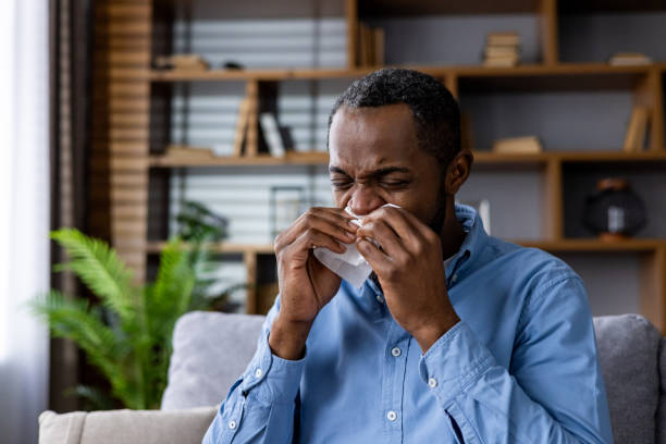 istock Man sneezing into tissue at home with flu symptoms 2164029220