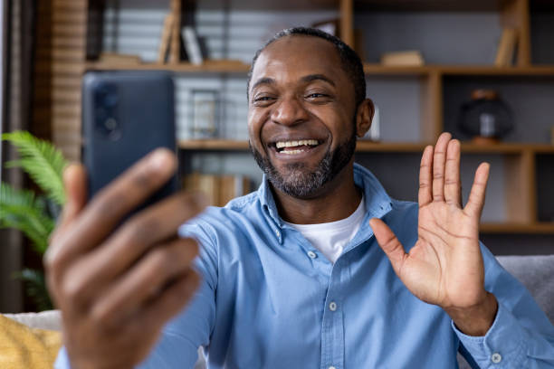 istock Smiling man making a video call and waving while sitting at home 2164029772