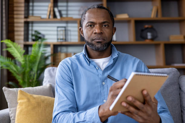 istock Mature man sitting on couch taking notes during video call in modern living room 2164030779