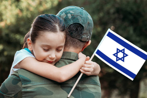Little girl hugs the soldier father and holding Israeli flag.