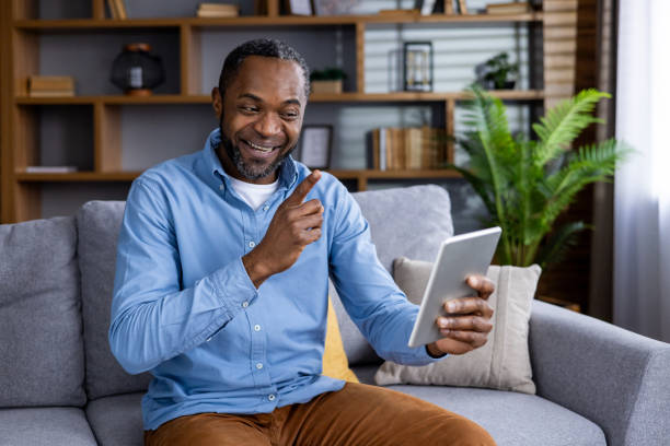 istock Happy man enjoying video call at home on digital tablet while sitting on sofa 2164032779