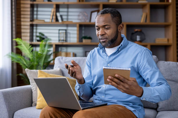 istock Man working remotely from home on laptop holding notebook having video call 2164033123