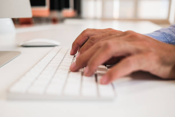 istock Modern Office Productivity - Hands on Wireless Keyboard. Person's hands typing on a white computer keyboard 2164034807