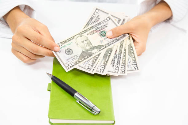 istock A woman's hand counting dollars, notebook and pen on the table 2164047187