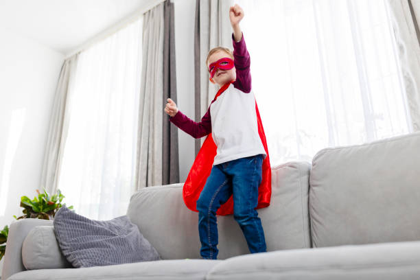 istock Boy in superhero costume standing on couch 2164048426